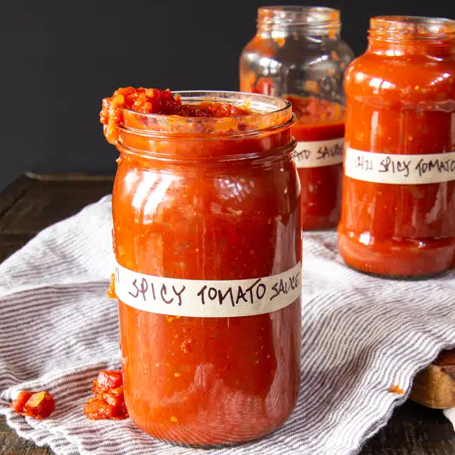 Three jars labeled spicy tomato sauce with a little dripping over the side.