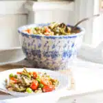 A plate of barley pilaf tossed with baby artichokes, tomatoes and spring peas, with a bowl of the pilaf in the background.