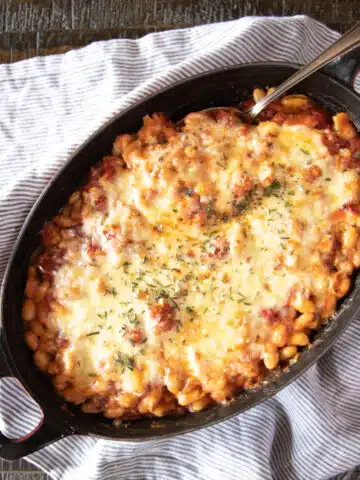 A baked bean and tomato casserole topped with cheese and rosemary.