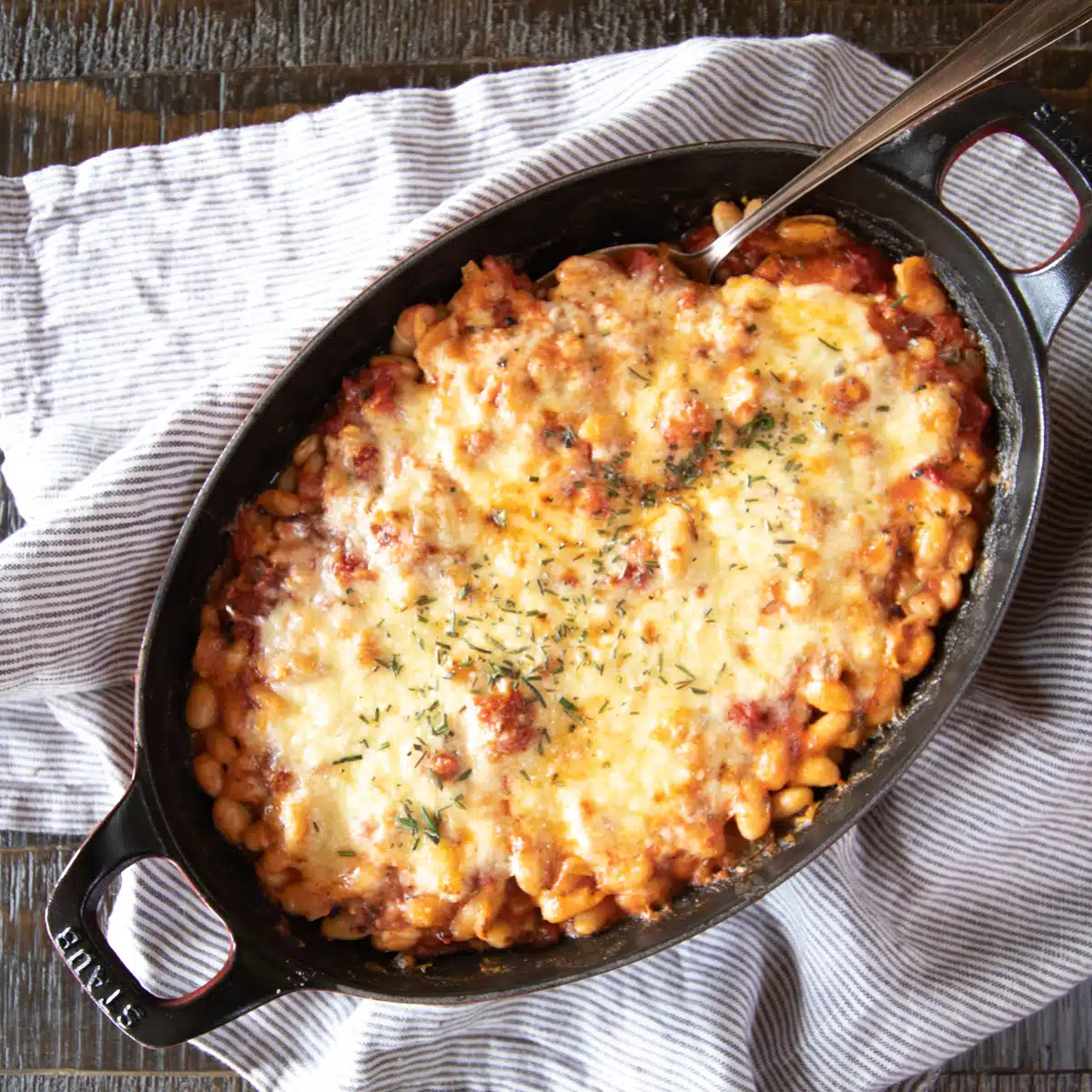 A baked bean and tomato casserole topped with cheese and rosemary.
