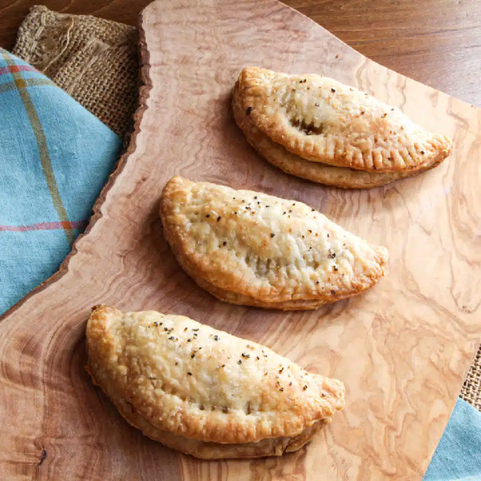 Three vegetarian Cornish pasties laid out on a cutting board.