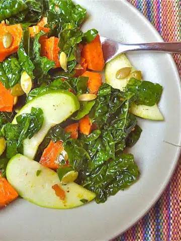 Kale salad with roasted sweet potatoes, apples and pepitas on a plate.