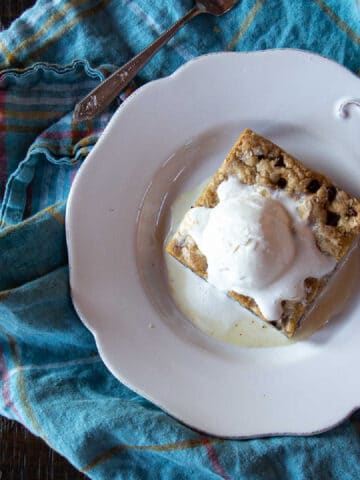 Chocolate chip cookie bar topped with a scoop of ice cream on a plate.