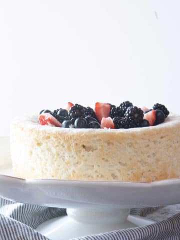 Angel food cake on a cake stand, topped with berries.