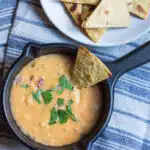 A small pot of chile con queso with corn chips.