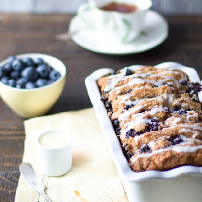 Blueberry scone loaf in a loaf pan, with butter and extra blueberries.