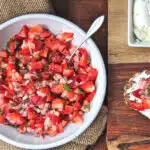 A bowl of fresh strawberry salsa with a crostini spread with cheese and topped with salsa.