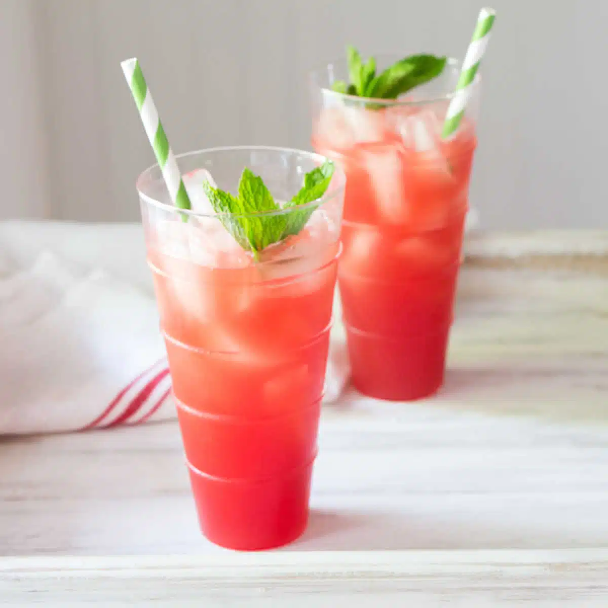 Two glasses of a watermelon wine cooler with mint and straws.
