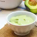 Small bowl of avocado cream, with a cut avocado in the background.