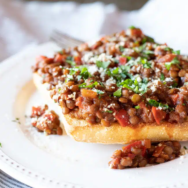 Lentil sloppy joe sauce ladled on top of a toasted rolls and topped with chopped parsley and Parmesan cheese.