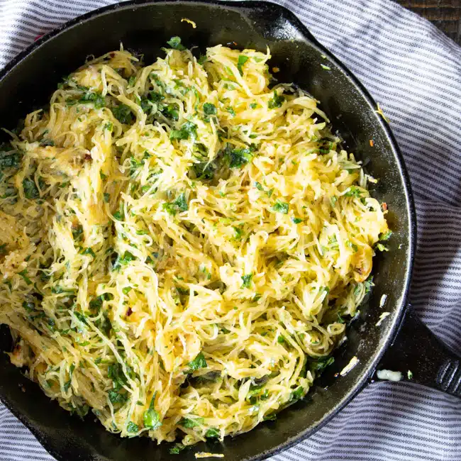 Cooked spaghetti squash sautéing in skillet with olive oil, garlic, red pepper flakes and parsley.