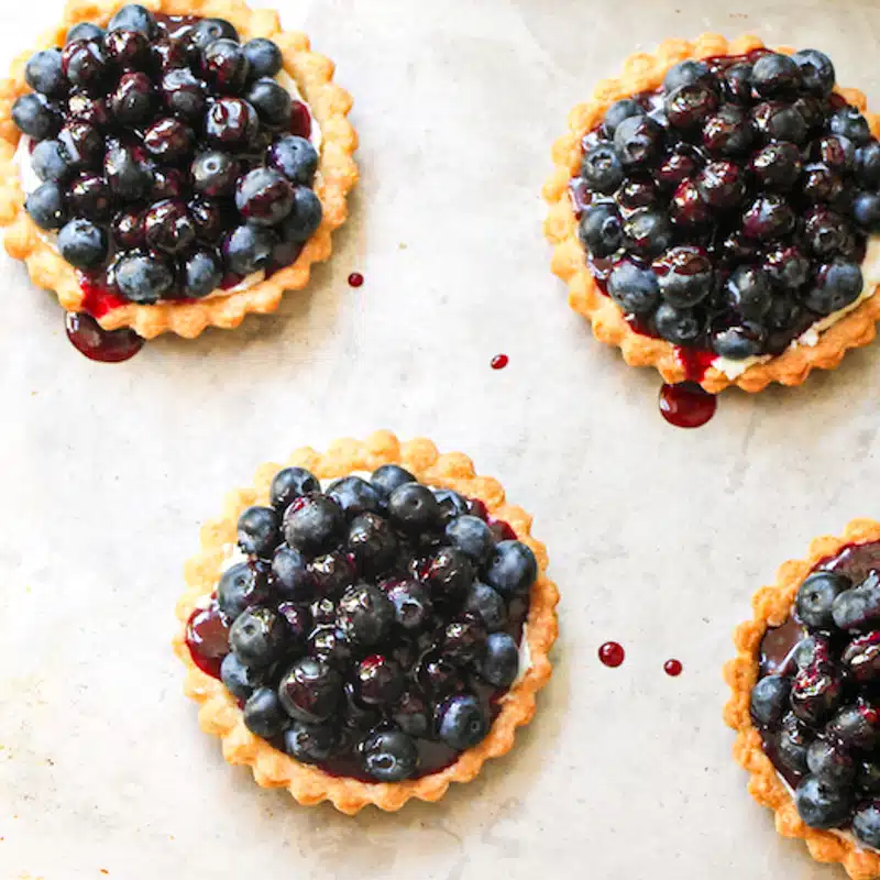 Top down view of glazed blueberry tartlets on parchment paper.