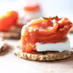Close up of fire roasted cherry tomatoes and feta cheese stacked on a cracker.