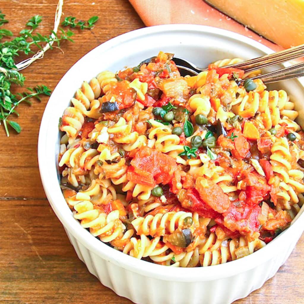 A serving bowl of Sicilian pasta dish of fusilli tossed with eggplant, tomatoes and capers.