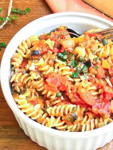 A serving bowl of Sicilian pasta dish of fusilli tossed with eggplant, tomatoes and capers.