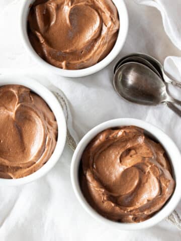 Three ramekins of chocolate mousse with three spoons.