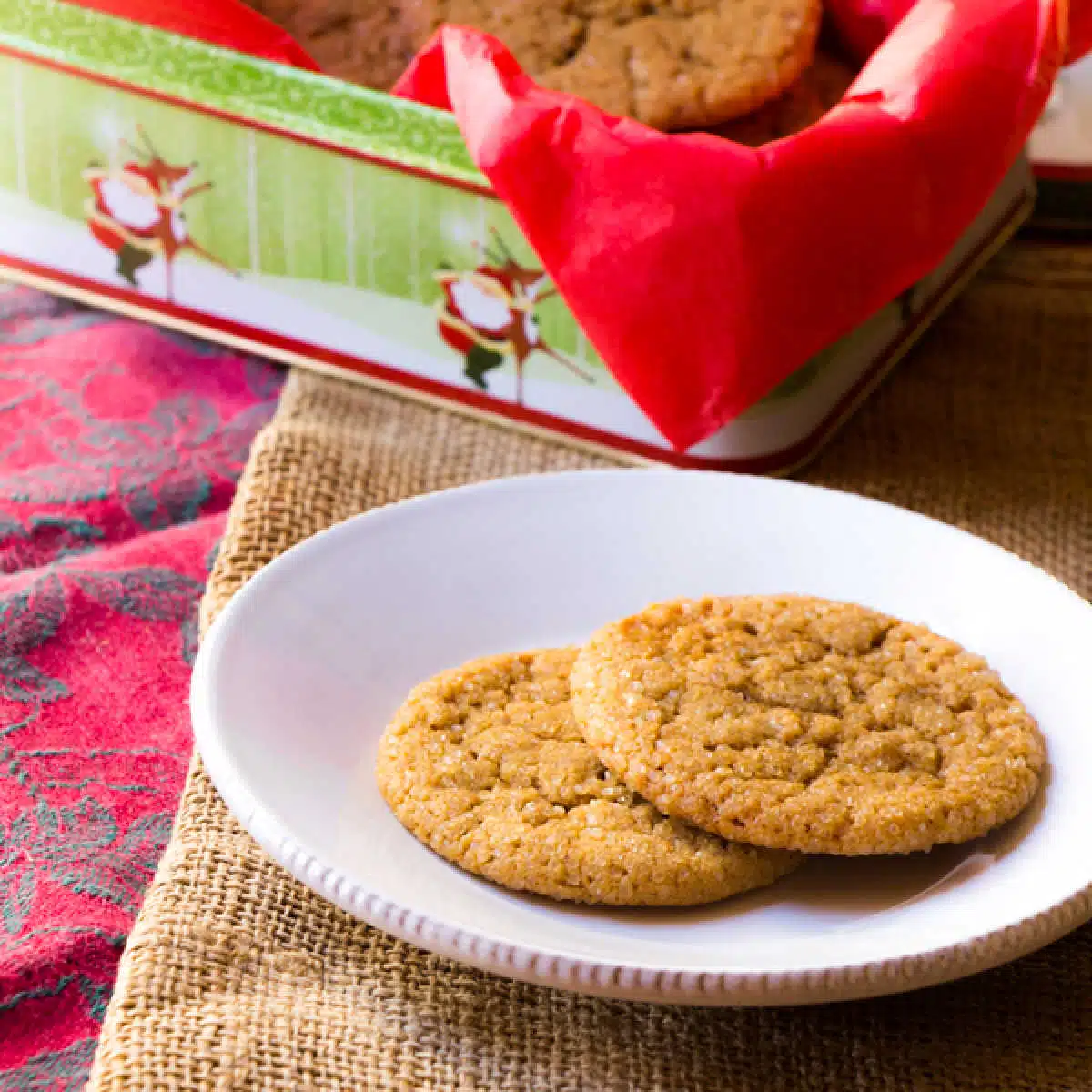 Two ginger molasses cookies on a plate with a box of cookies in the background.