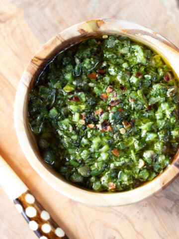 A wooden bowl of cilantro chimichurri with red pepper flakes on a cutting board.