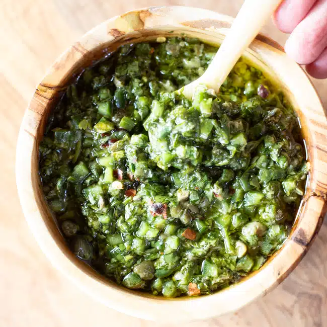 A bowl of cilantro chimichurri with a spoon lifting up some of the sauce.