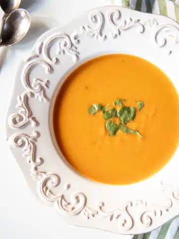 A bowl of carrot coconut and ginger soup topped with a little cilantro.