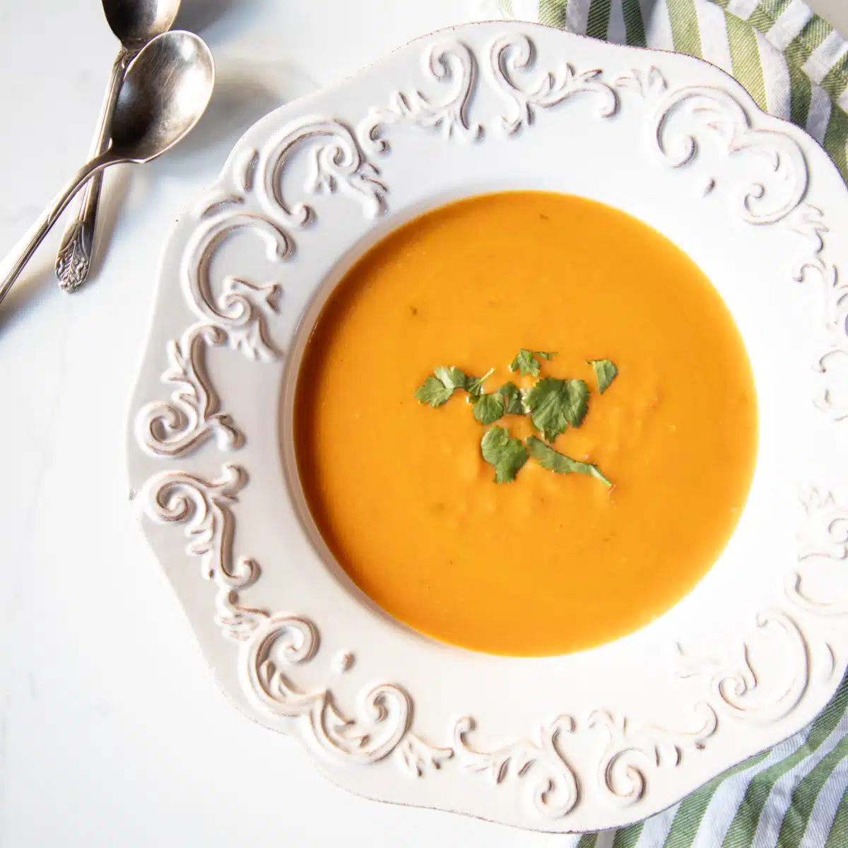 A bowl of carrot coconut and ginger soup topped with a little cilantro.