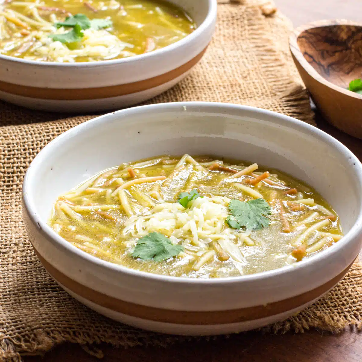 Two bowls of Mexican spaghetti soup topped with grated cheese.