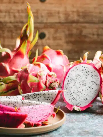 Whole dragon fruit with some cut up on a plate.