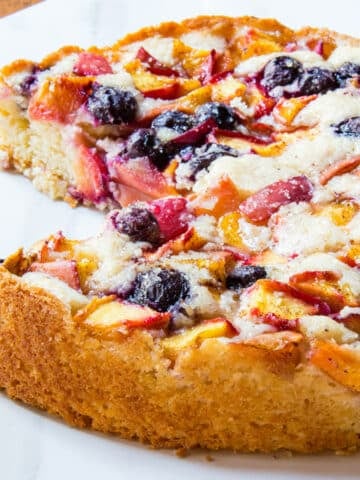 Summer peach cake topped with fresh peaches and blueberries on a marble counter.