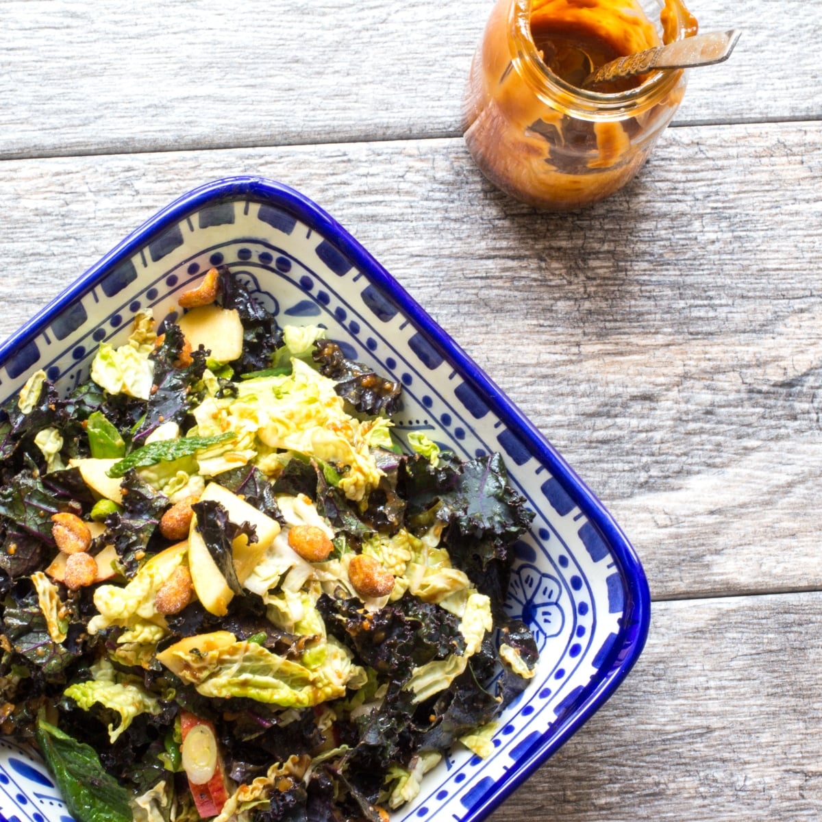 A bowl of kale and apple salad with a jar of Thai peanut butter dressing