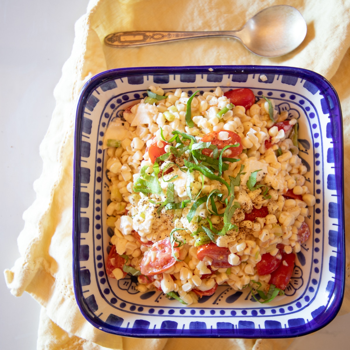 A blue bowl filled with simple corn and tomato salad topped with slivers of basil.