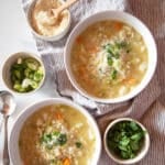Two bowls of vegetable rice soup with condiments on the side.