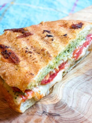 One half of a sliced caprese panini on a cutting board.