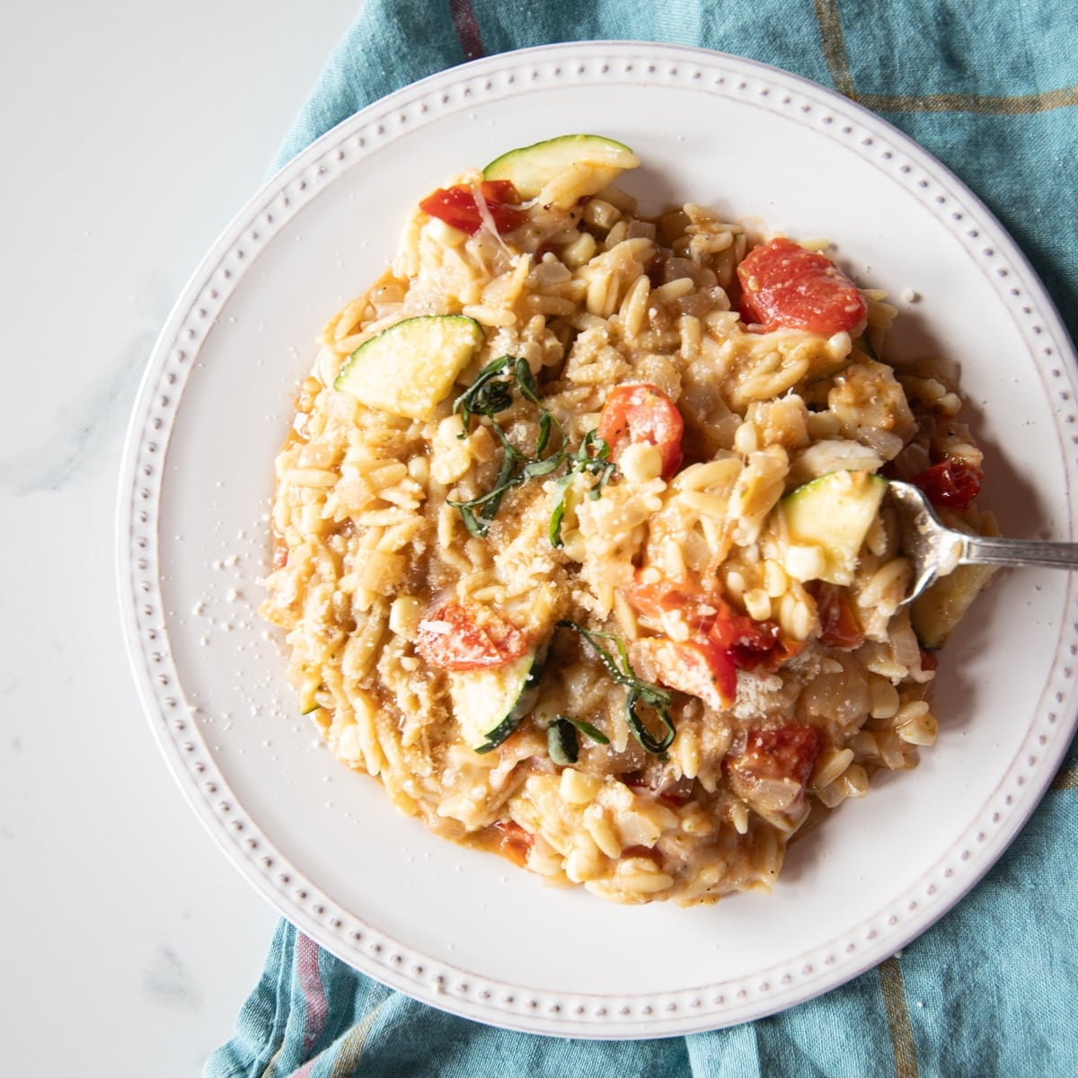 One-pot pasta dish of tomatoes, zucchini, corn, pesto, and mozzarella mixed into orzo on a white plate.
