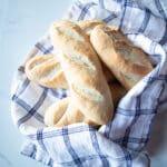 Several mini baguettes wrapped in a blue and white tea towel.