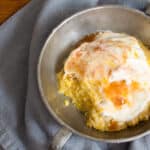 A scoop of polenta cake in a silver bowl topped with honey yogurt and peach preserves.