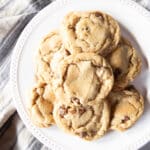 A pile of chubby chewy chocolate chip cookies on a white serving plate.