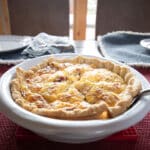 A ceramic dish filled with a simple quiche with a set table in the background.