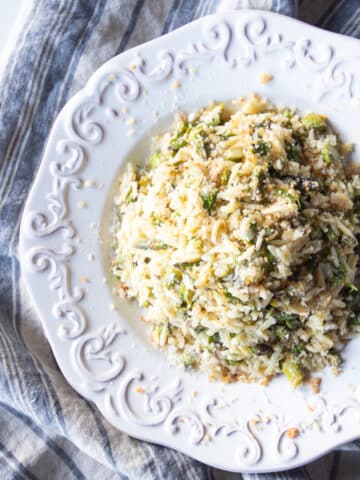 A white pasta bowl filled with lemony orzo and asparagus with breadcrumbs.